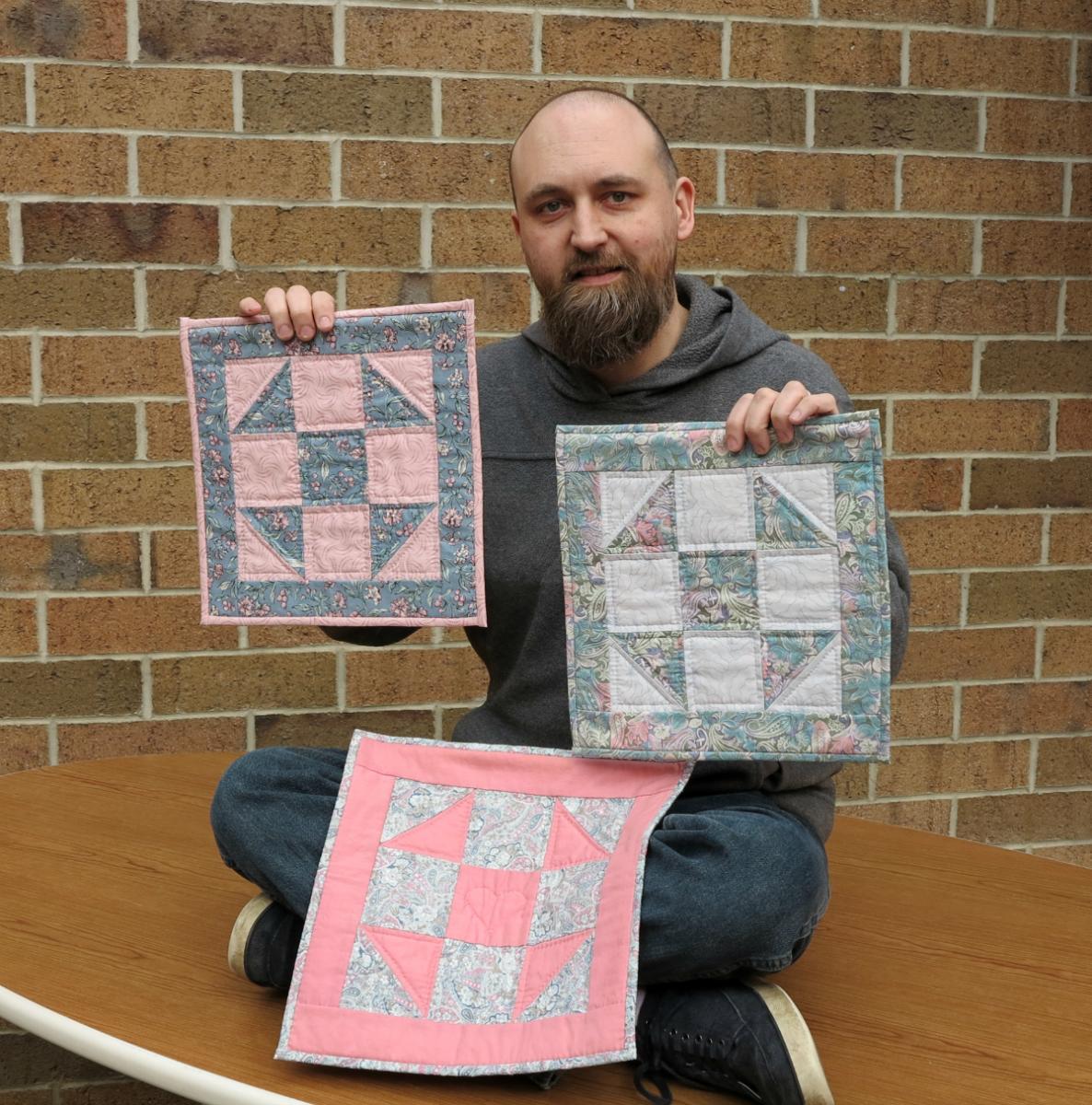 Cat's Meow staffer, Chris, holding his mother's Shoo Fly Quilt blocks created in her quilting class.