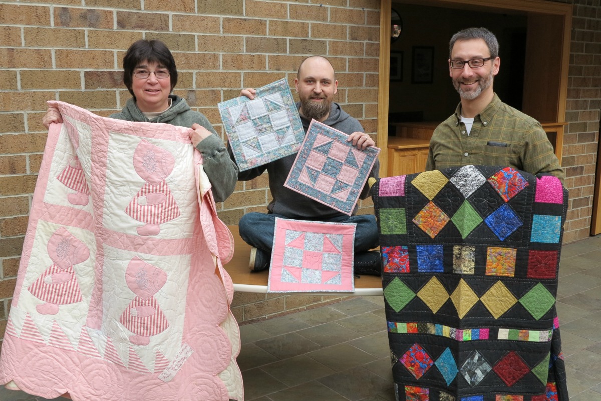 Cat's Meow staff members, Danette, Chris, and Brent holding their family quilts